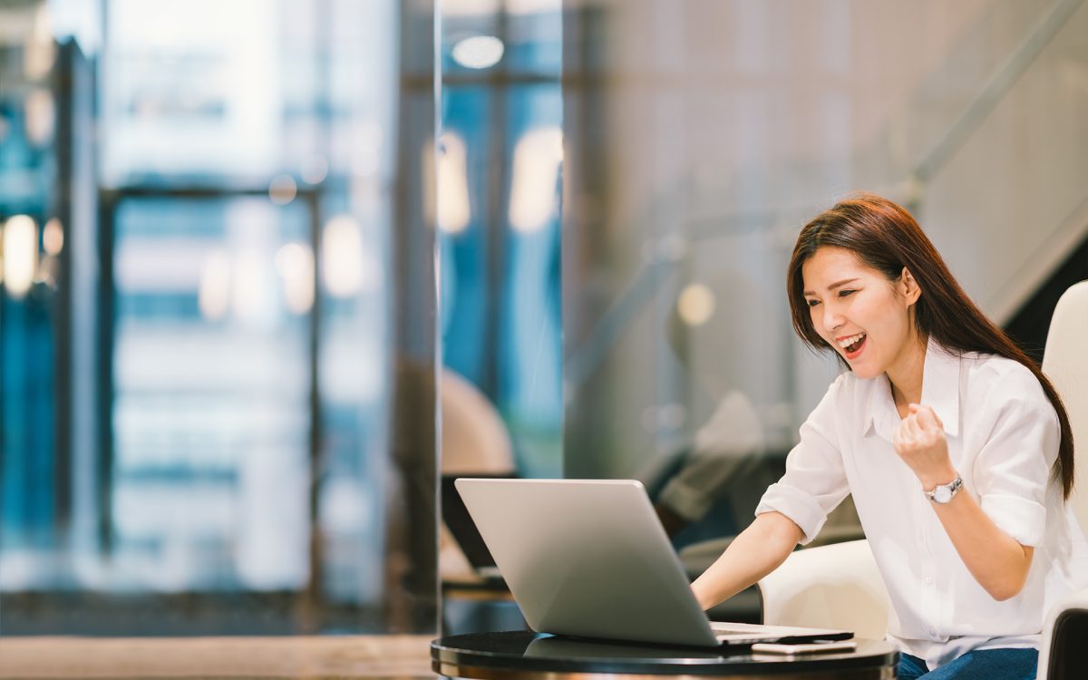 Beautiful Asian girl celebrate with laptop, success happy pose. E-commerce, university education, internet technology, or startup small business concept. Modern office or living room with copy space